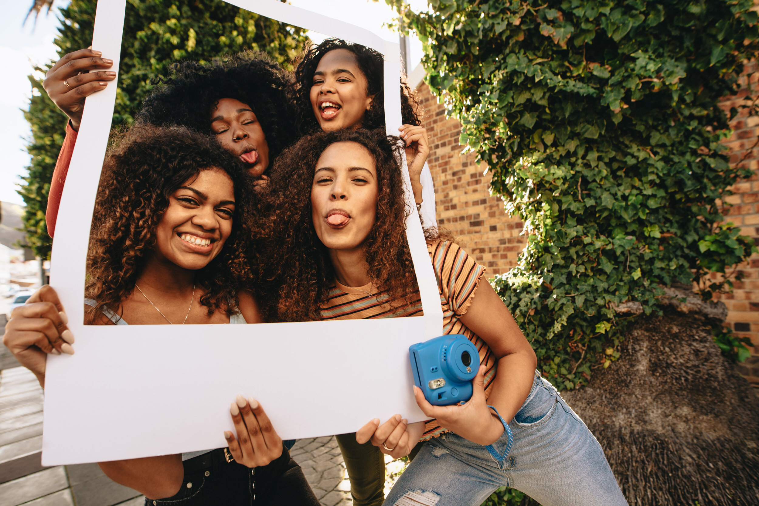 Black women taking a photo together in a life-sized polaroid frame